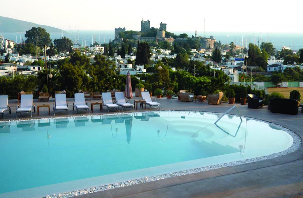a swimming pool with chairs and a city in the background at Lvzz Hotel in Bodrum City