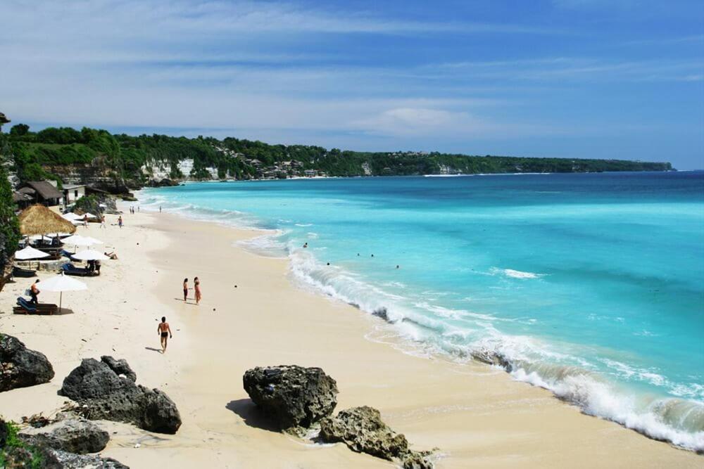 a beach with people on the sand and the ocean at Les chalets Uluwatu in Uluwatu