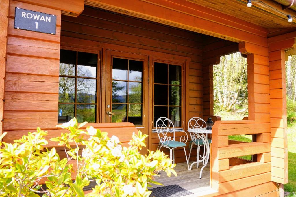 un porche de una cabaña de madera con mesa y sillas en Cosy Rowan woodland lodge no1, en Killin