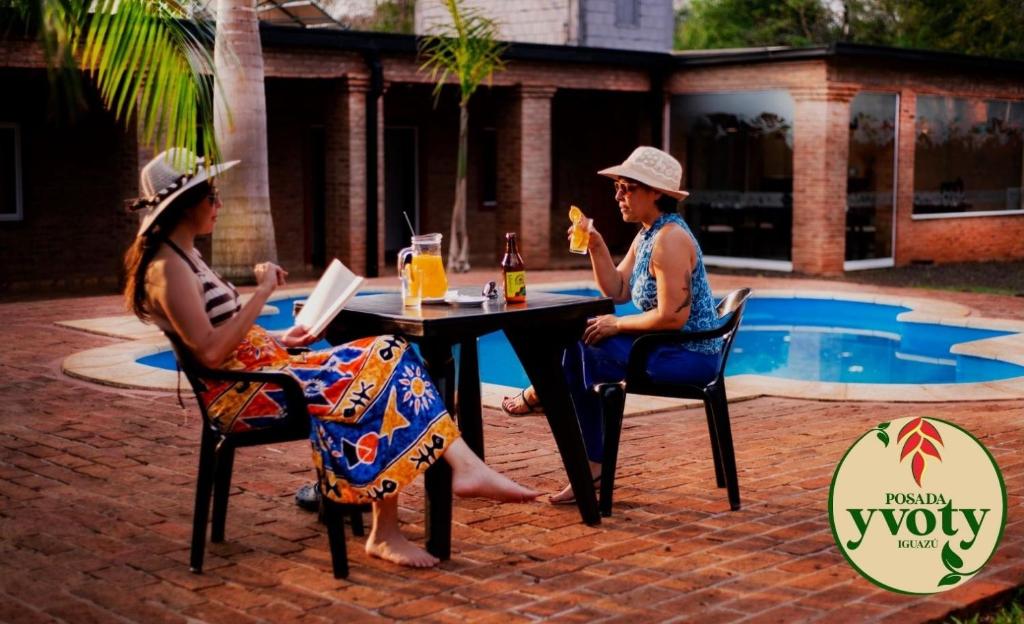 zwei Personen sitzen an einem Tisch in der Nähe eines Pools in der Unterkunft Posada Yvoty in Puerto Iguazú