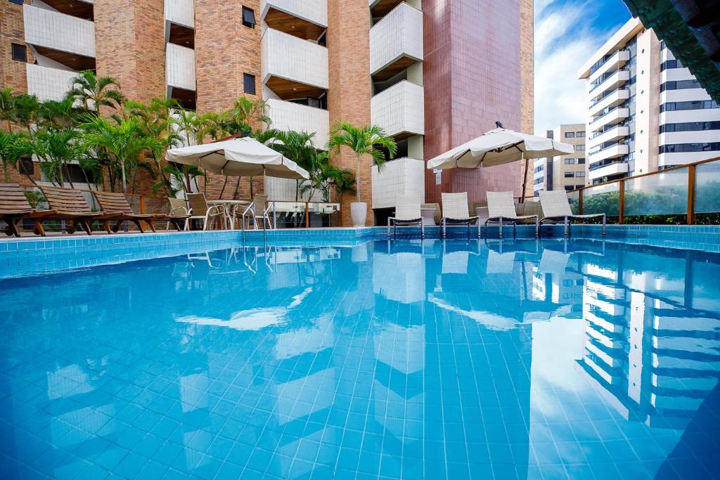 a swimming pool with chairs and umbrellas next to a building at San Marino Suite Hotel in Maceió