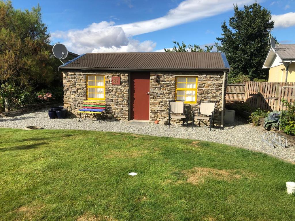 una pequeña casa de piedra con sillas y un patio en Fache Cottage, en Clyde