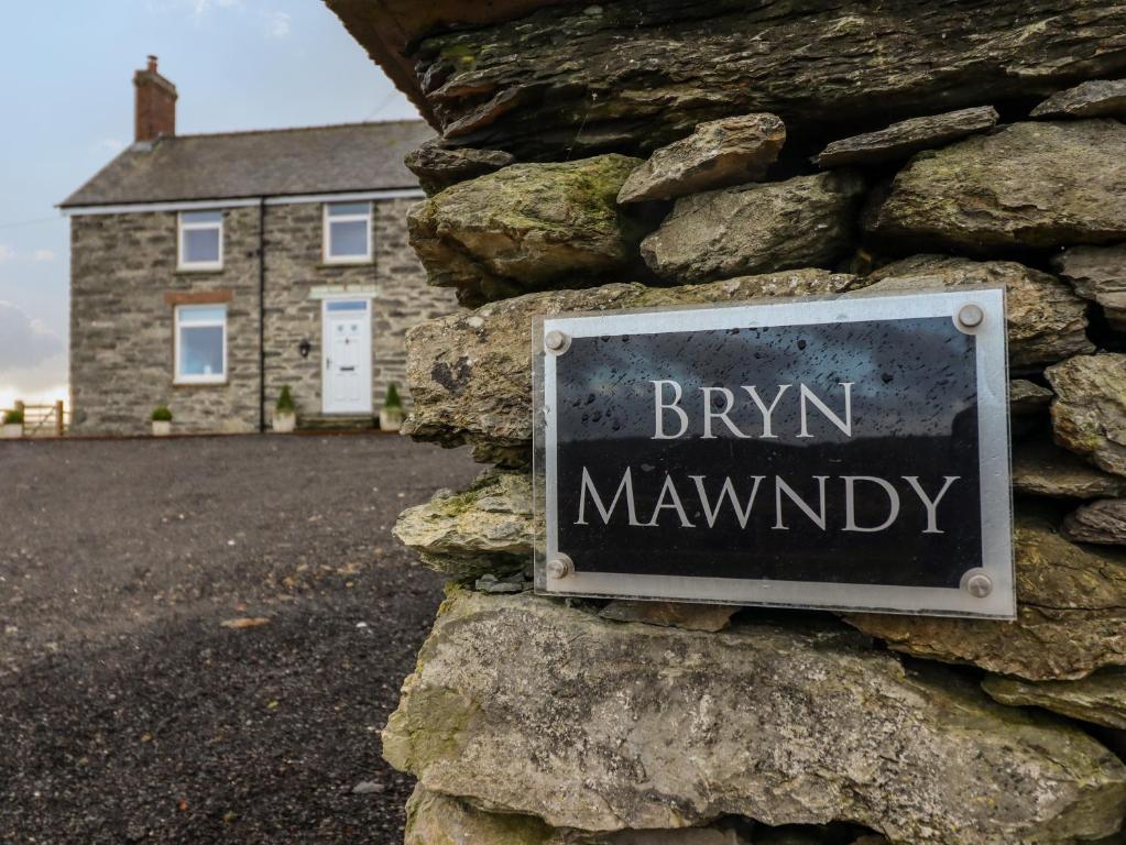 a sign on the side of a stone wall with a brick house at Bryn Mawndy in Corwen