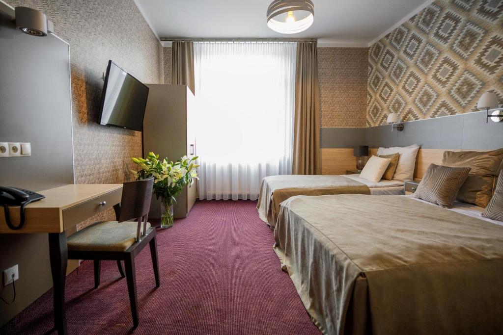 a hotel room with two beds and a desk and a window at Hotel Kazimierz in Kraków