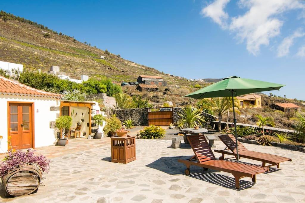 um pátio com 2 cadeiras e um guarda-sol verde em Casa La Time em Fuencaliente de la Palma