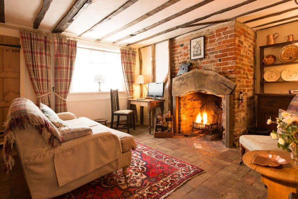 a living room with a fireplace and a couch at Spadgers, a flax workers cottage next to fields in a Medieval Village in Long Melford