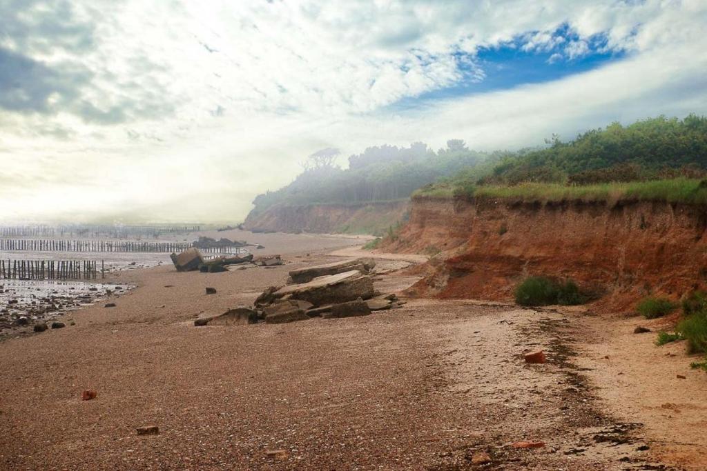 a beach with a rocky shoreline and a cliff at Bromans Barn a beautiful cottage by the Sea and Cudmore Nature Reserve in West Mersea