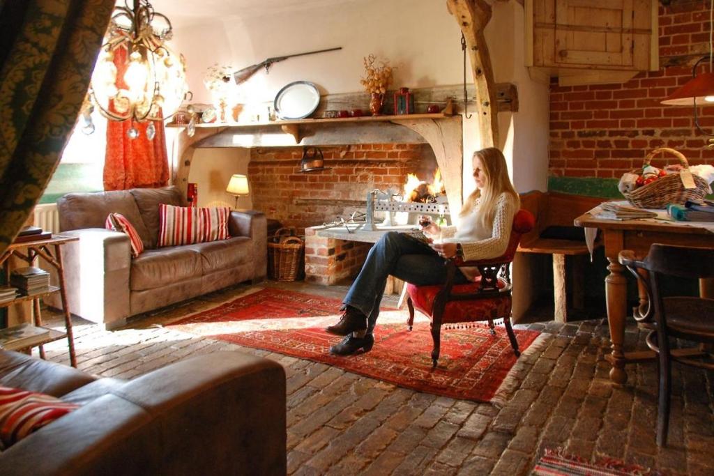 a woman sitting in a chair in a living room with a fireplace at Orchard Cottage cosy rustic comfort just across the fields to a great Pub 