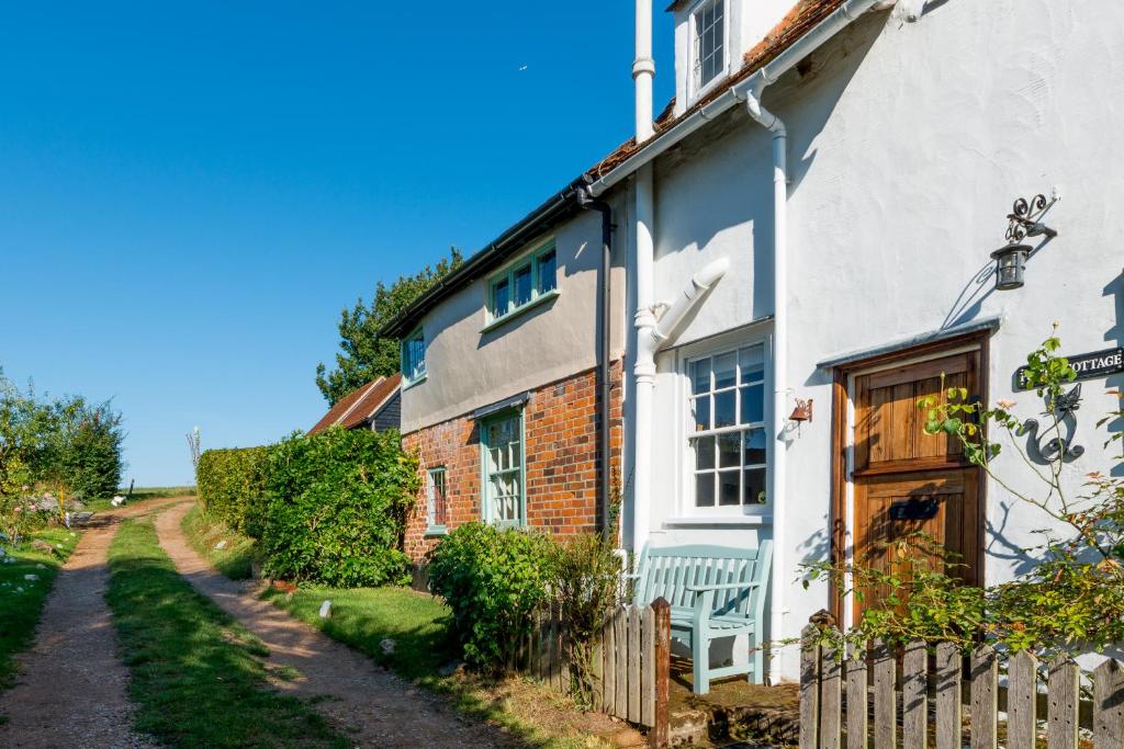 a white house with a wooden door and a fence at Putts Cottage hidden away at the end of a cart track, happily lost in Sudbury