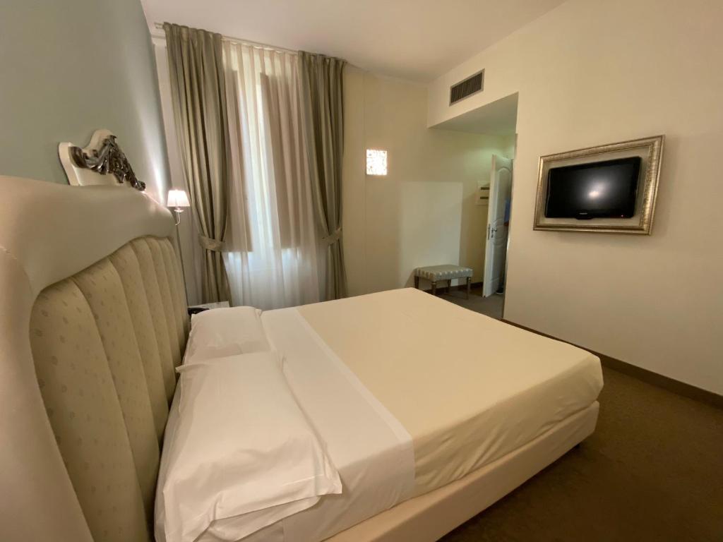 um quarto de hotel com uma cama branca e uma televisão em JR Hotels Oriente Bari em Bari