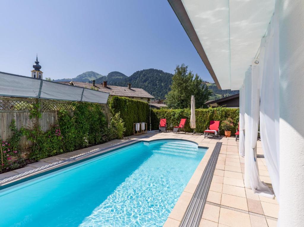 a swimming pool with red chairs and a house at Landhaus Central in Söll