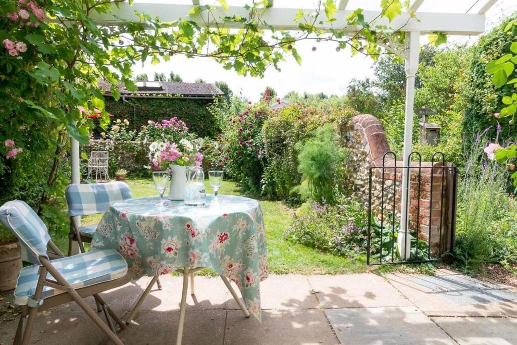 une table et des chaises dans un jardin avec une pergola dans l'établissement Romney, a cosy Victorian cottage in a picturesque Suffolk village, à Cavendish