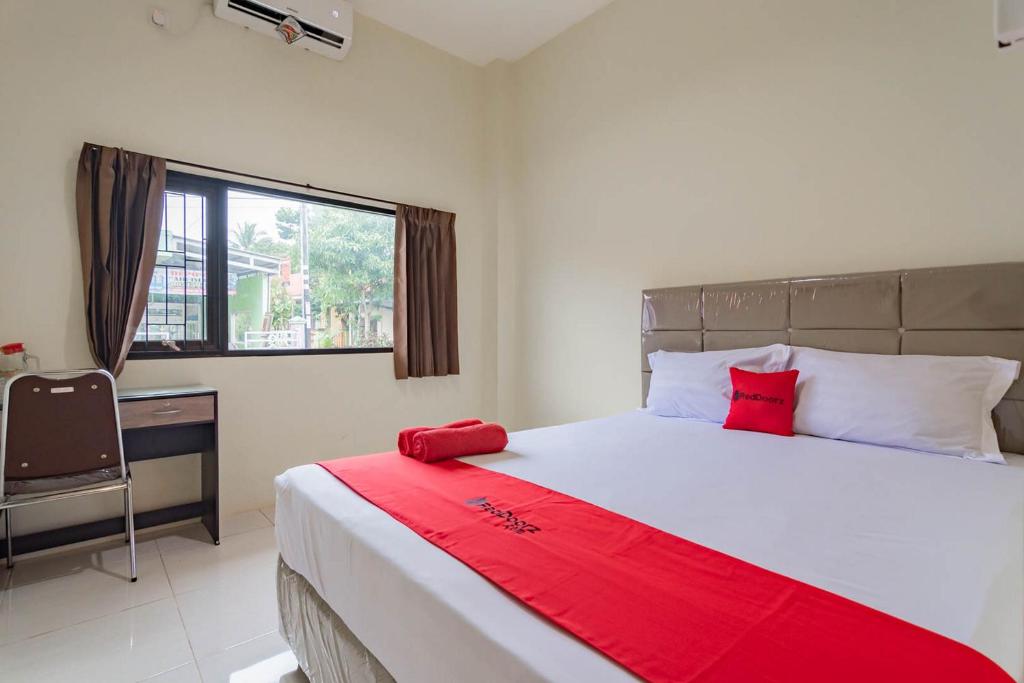um quarto com uma cama grande com lençóis vermelhos e uma janela em RedDoorz near Arka Sepinggan Airport em Balikpapan