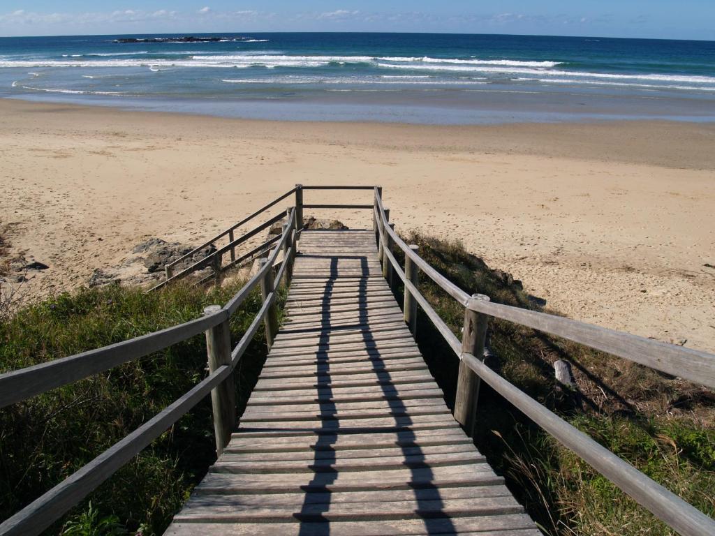 a wooden boardwalk leading to a beach with the ocean at Safety Beach Ocean Bungalows in Woolgoolga