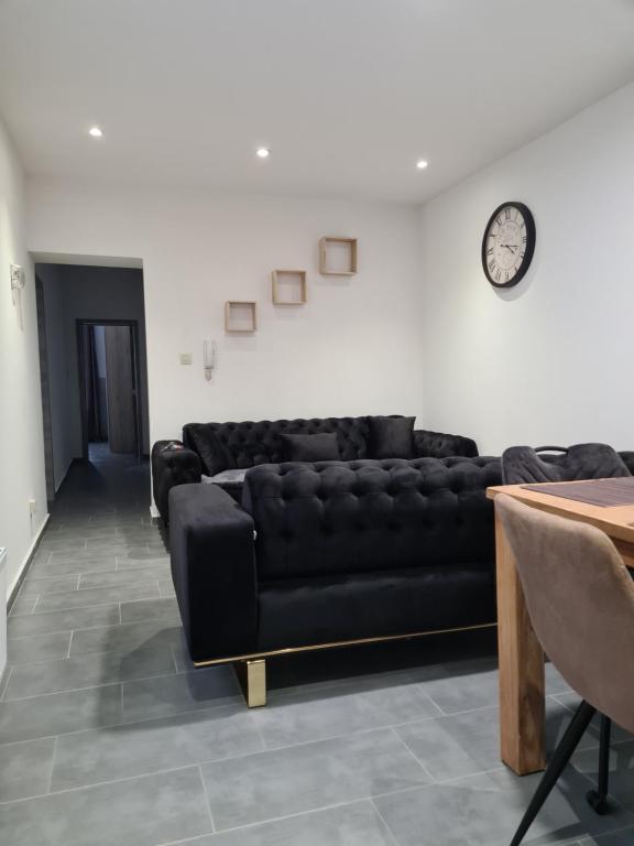 a living room with a black leather couch and a clock at Harmonie 2 chambres parking et wifi gratuits in Charleroi