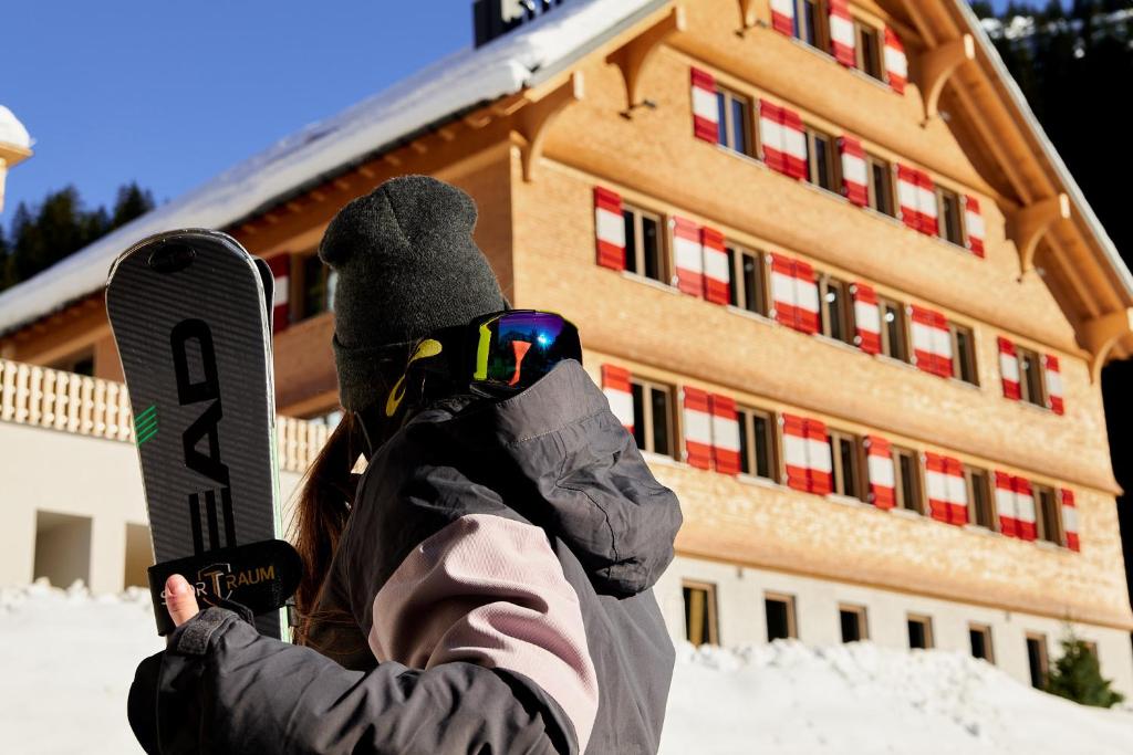 a person holding a snowboard in front of a building at Berghaus Schröcken - Hotel Apartments Spa in Schröcken
