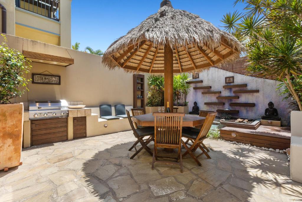 eine Terrasse mit einem Tisch und einem Strohschirm in der Unterkunft Villa Baci Nobby Beach in Gold Coast