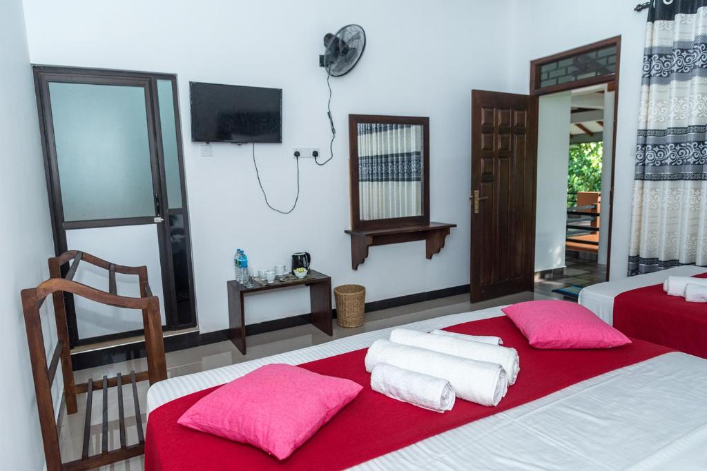 a bedroom with two beds with red sheets and pink pillows at Sadee's Place in Dambulla