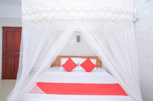 un letto a baldacchino bianco con cuscini rossi sopra di Hotel Cranberry a Hikkaduwa