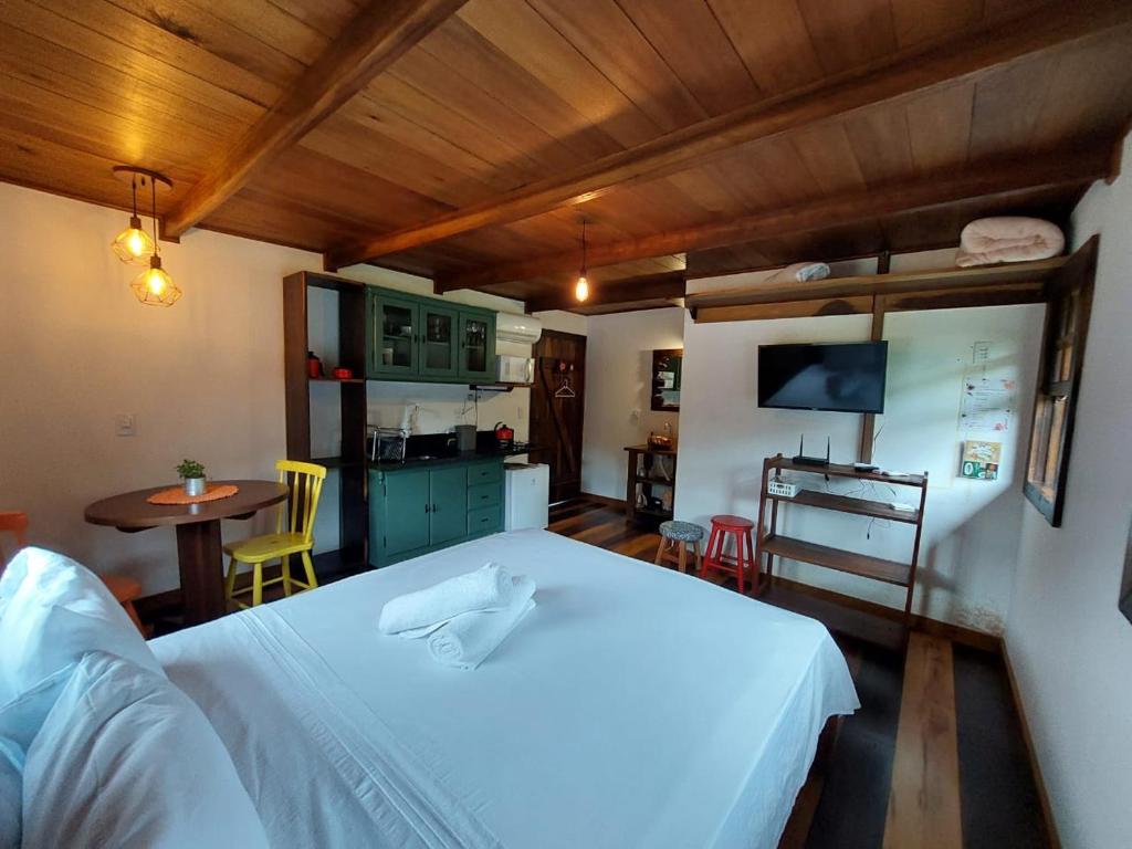 a bedroom with a white bed and a kitchen at Caminhos da Serra do Tabuleiro - Chalé do Lago in São Bonifácio