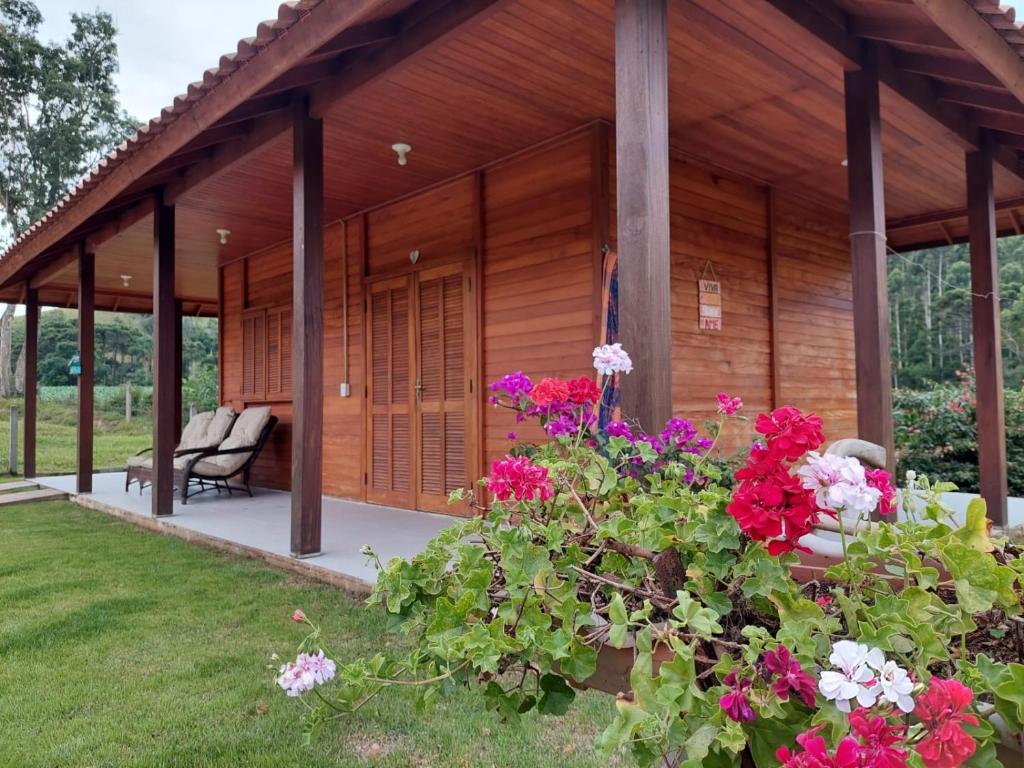 une cabane en bois avec des fleurs devant elle dans l'établissement Caminhos da Serra do Tabuleiro - Chalé Araucária, à São Bonifácio