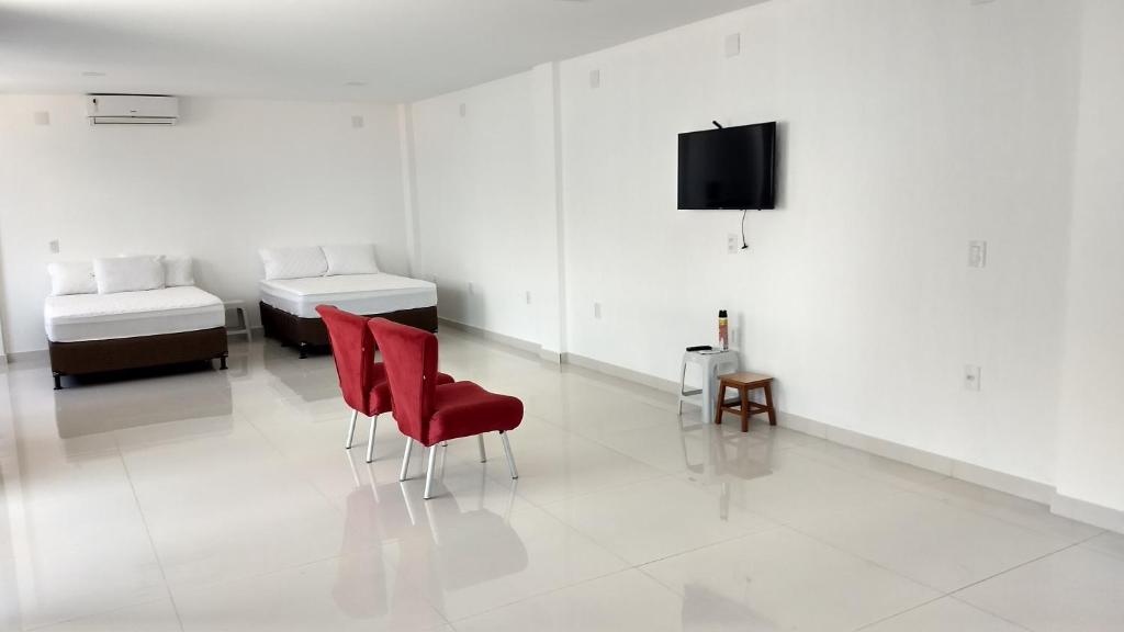 ein weißes Zimmer mit 2 Betten und einem roten Stuhl in der Unterkunft Suítes Cabo Frio in Cabo Frio