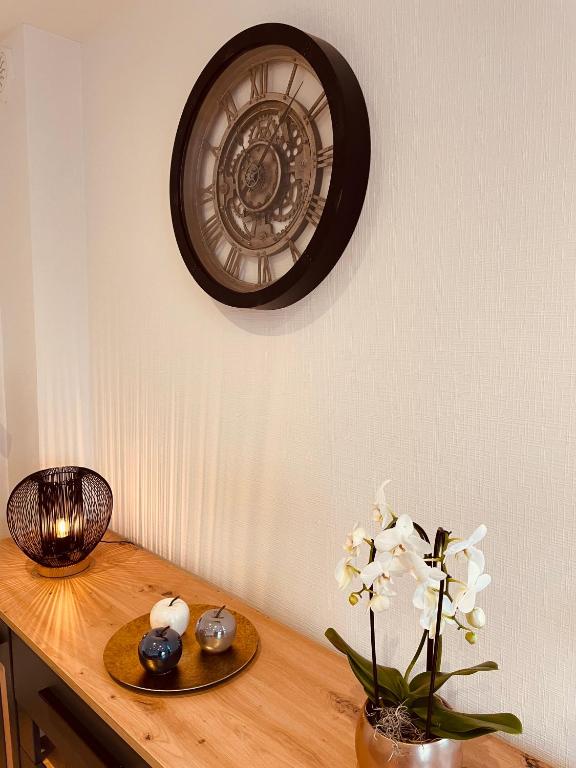 a clock on a wall above a wooden table with flowers at Appartement Les Tilleuls &quot;3 étoiles&quot; in Niederbronn-les-Bains