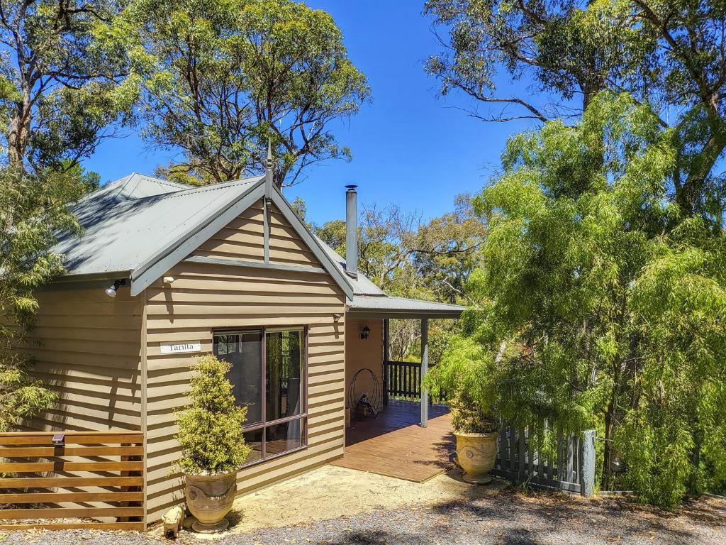 a small wooden house with a porch and trees at Tarilta Cottage in Hepburn Springs