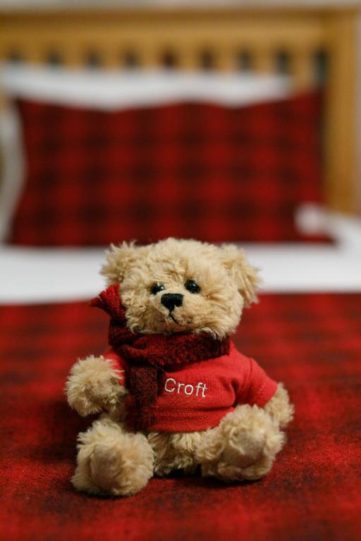 a teddy bear wearing a red shirt sitting on a bed at Ceol na Mara Guest House in Tarbert