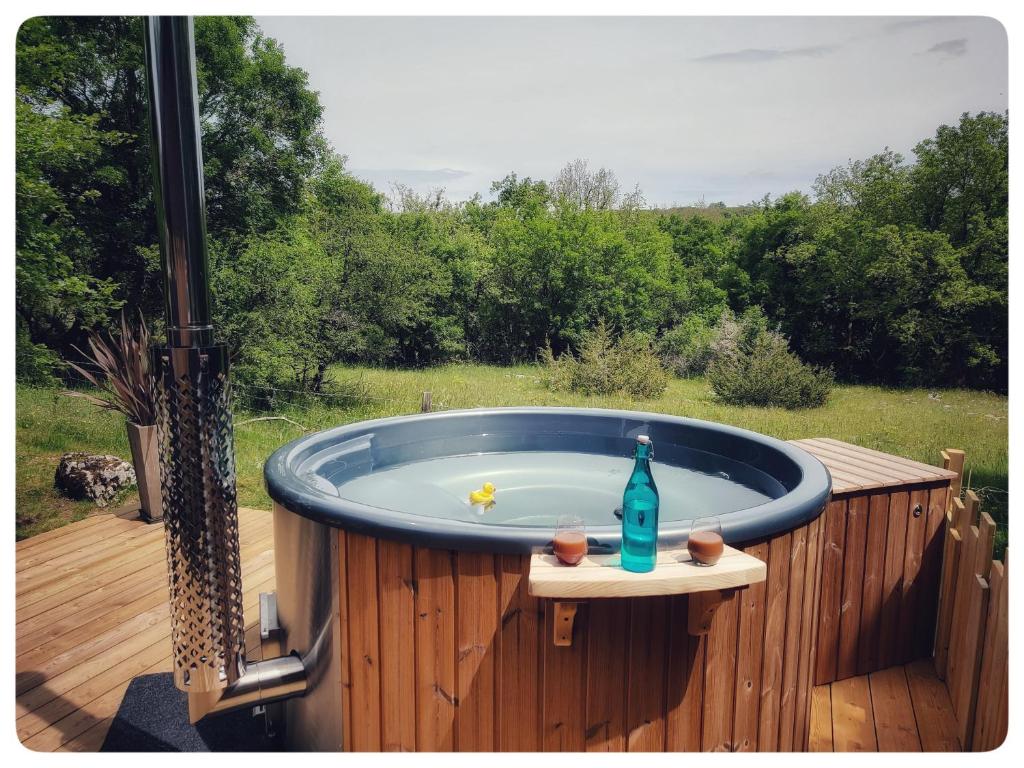 bañera de hidromasaje con botella en una terraza de madera en Chalet, bain nordique (spa) dans le triangle noir en Quissac