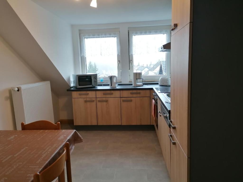 a kitchen with wooden cabinets and a table and two windows at Ferienwohnung Yara Rödental in Rödental