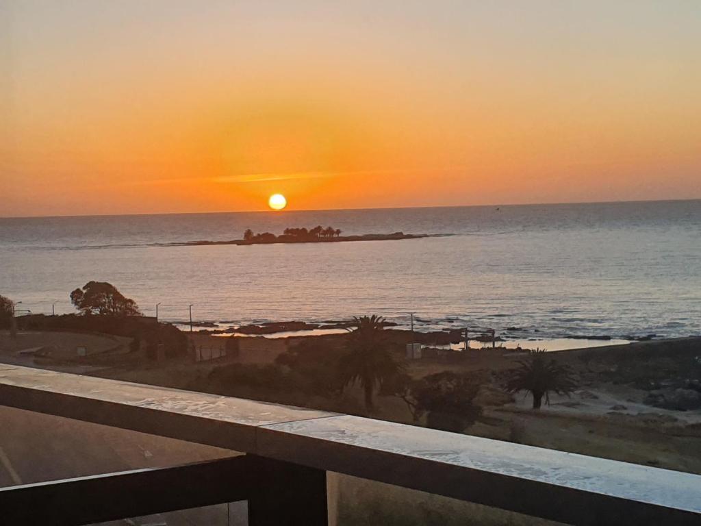 einen Sonnenuntergang über dem Meer mit einer Insel im Wasser in der Unterkunft Modern apartment first line beach Montevideo UY in Montevideo
