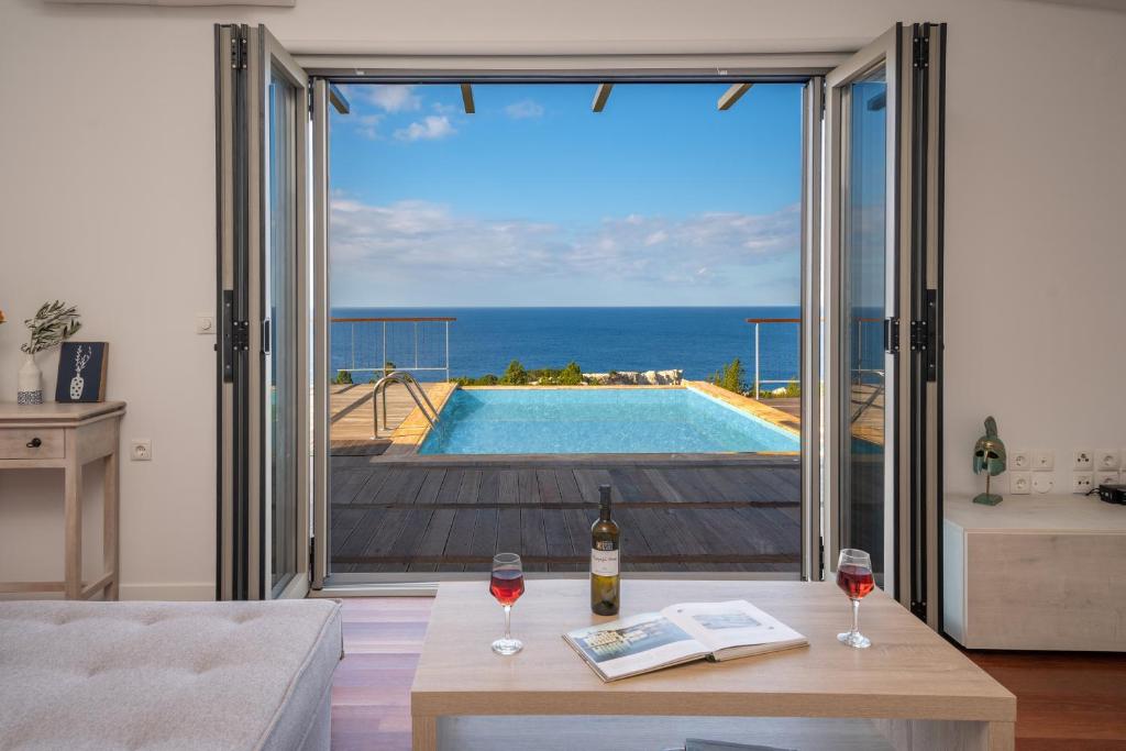 a living room with a view of a pool and a table with wine glasses at Baklava Villa in Fiskardho