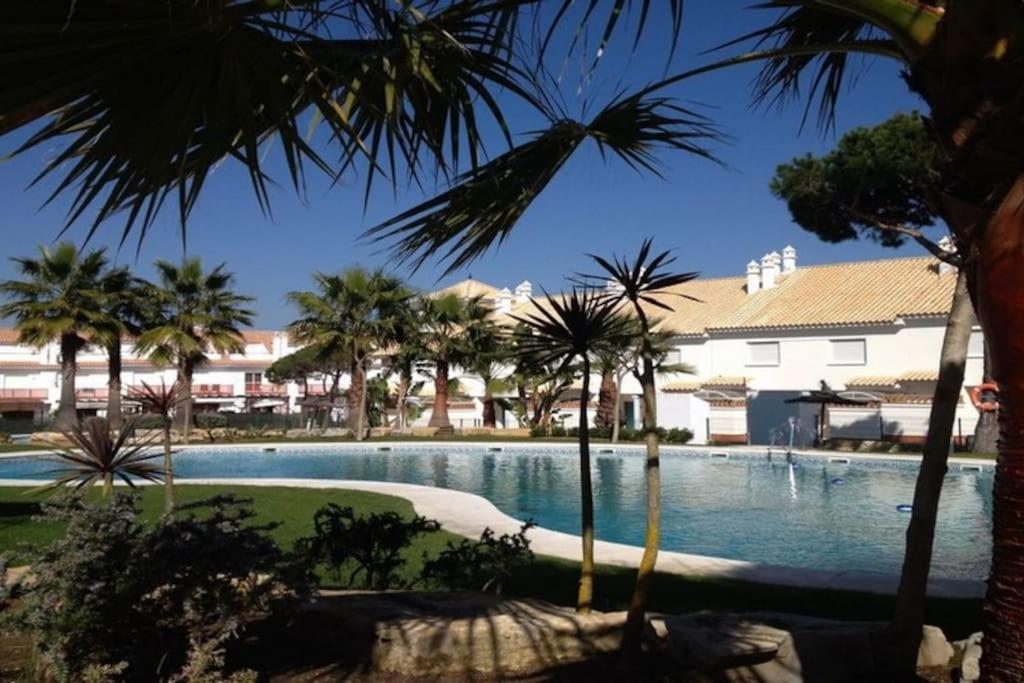 a swimming pool with palm trees in the foreground at Casa de lujo en la playa frente al campo de golf in El Portil
