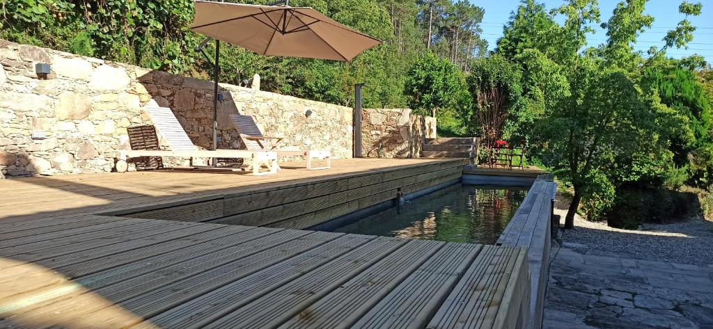 a wooden deck with an umbrella and a pond at Casa de Ribadafonte in Outes