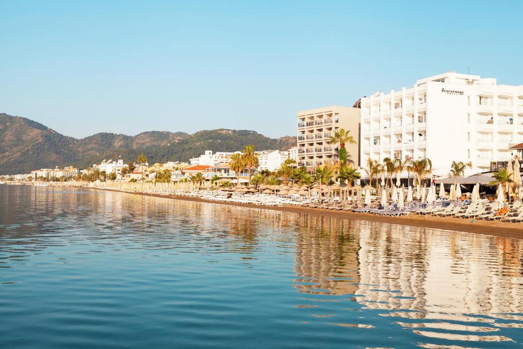 a beach with chaise lounges and palm trees and buildings at The Beachfront Hotel Adult Only 16 Plus in Marmaris