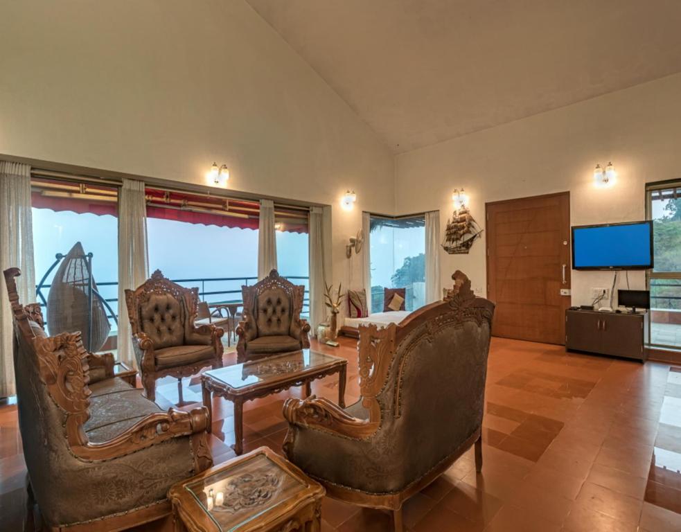 a living room with chairs and a table and a television at SaffronStays Aurelia, Panchgani - Balinese villa with breathtaking valley views in Panchgani