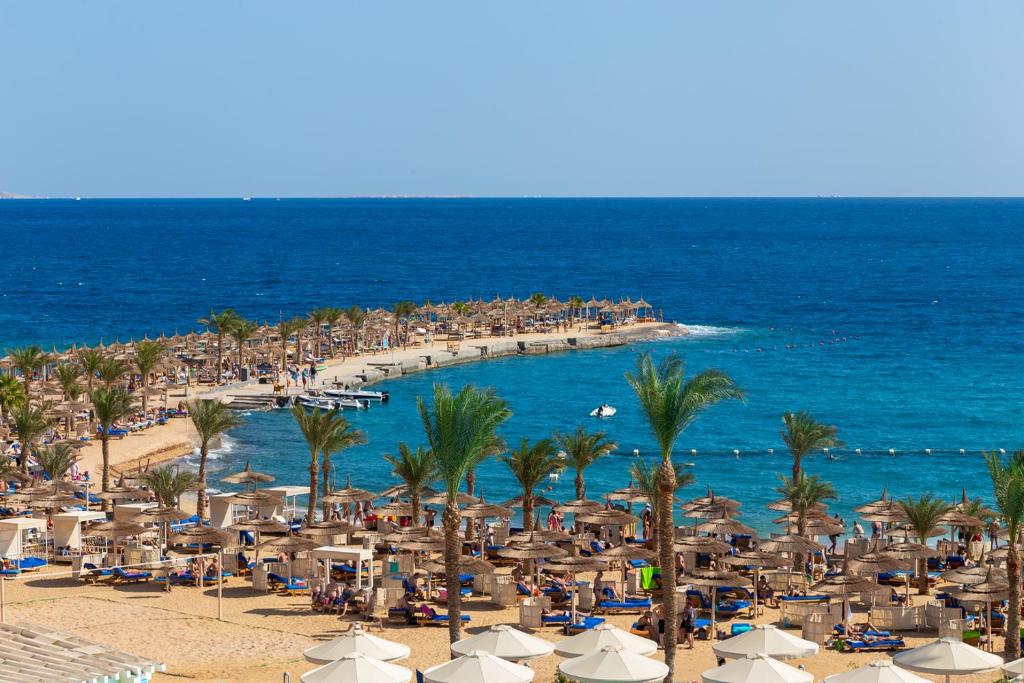 een strand met parasols en palmbomen en de oceaan bij Beach Albatros The Club - Aqua Park in Hurghada
