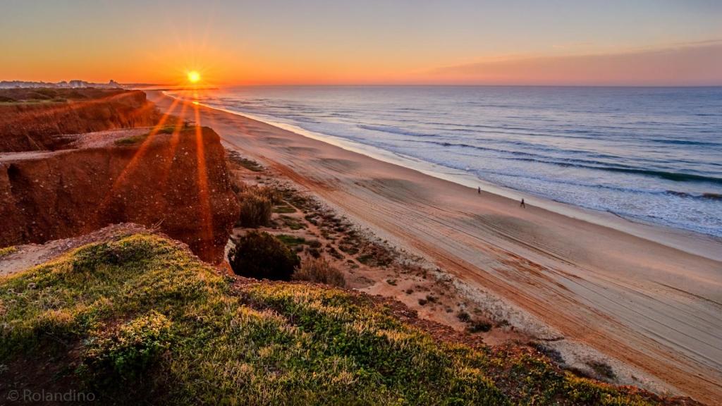 a beach with the sun setting over the ocean at Apartamento Medusa by Sunnyway in Olhos de Água