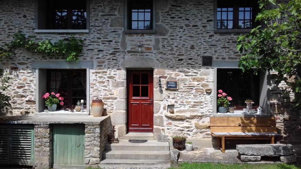 a stone house with a red door and a bench at Le Mas Bellanger in Saint-Pierre-Chérignat