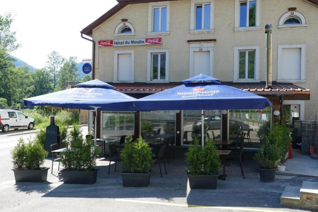 twee blauwe paraplu's voor een gebouw bij Hotel Restaurant du Moulin in Fleurier