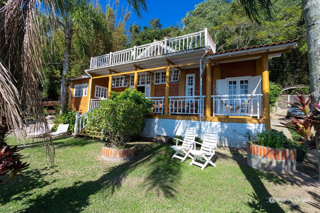 una casa amarilla con dos sillas en el patio en Recanto das Bromelias, en Laguna