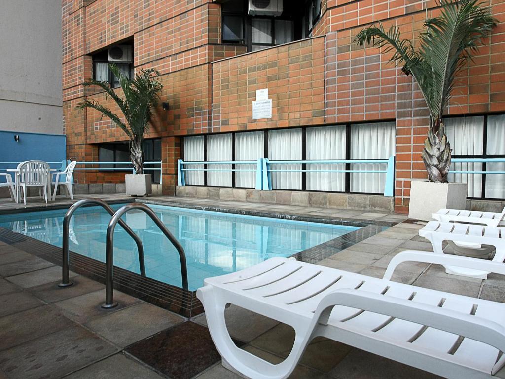 a swimming pool with two white benches next to a building at Cheverny Apart Hotel in Belo Horizonte