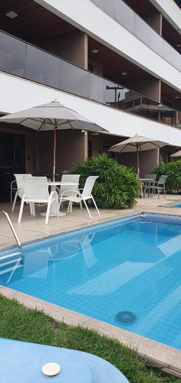 a pool with chairs and umbrellas next to a building at Porto Central Residence 01 in Porto De Galinhas