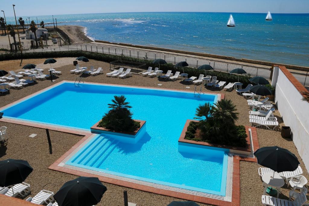 a swimming pool with chairs and umbrellas and the ocean at Residence Hotel Antica Perla in San Leone