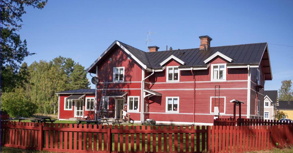 a red house with a black roof behind a red fence at Furudals Vandrarhem och Sjöcamping in Furudal
