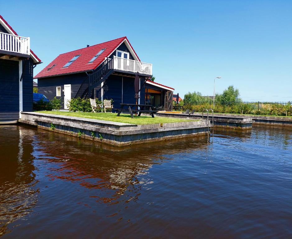 a house with a red roof sitting next to a river at Het Schiphuis met privé haven in Heeg