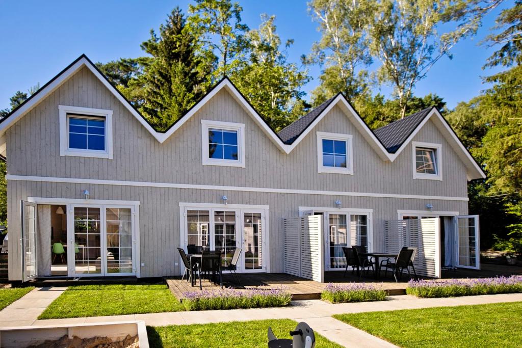 a white house with black chairs in the yard at Domki Na Brackiej in Pobierowo