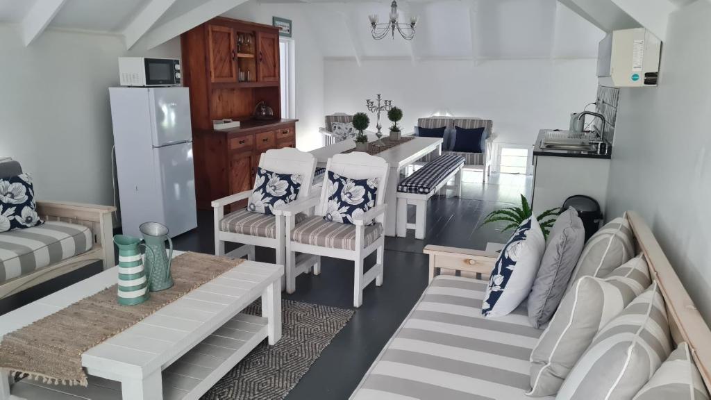 a living room with white chairs and a kitchen at Be Our Guest Self Catering in Nelspruit