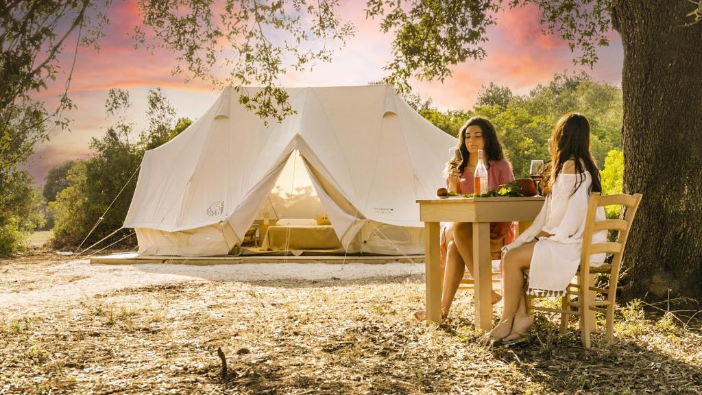 曼杜里亞的住宿－Cuturi Wine Glamping，两个女人坐在帐篷前的桌子上
